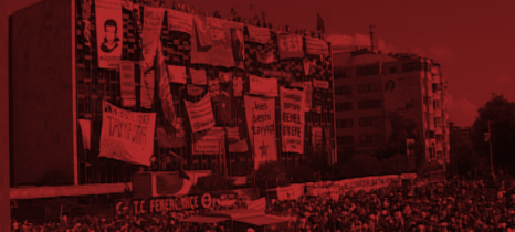 Mit Bannern vollgehängtes großes Gebäude am Taksim Platz in Istanbul, Mensvhen stehtn auf dem Dach, im Vordergrund eine dichte Menschenmasse
